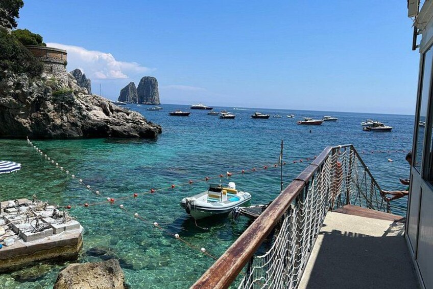 A coastal scene with boats, clear water, rocky outcrops, and a wooden walkway. 3