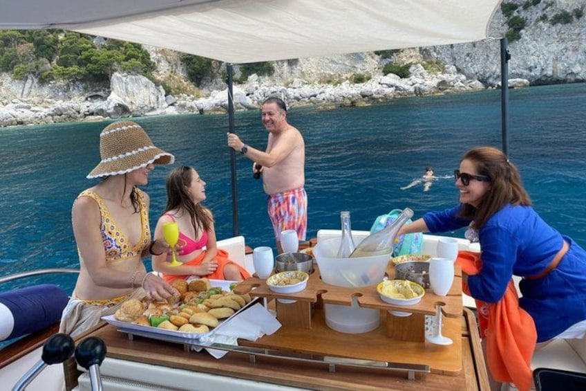 A group of people on a boat with a table set for a meal, surrounded by water and rocky cliffs. 4