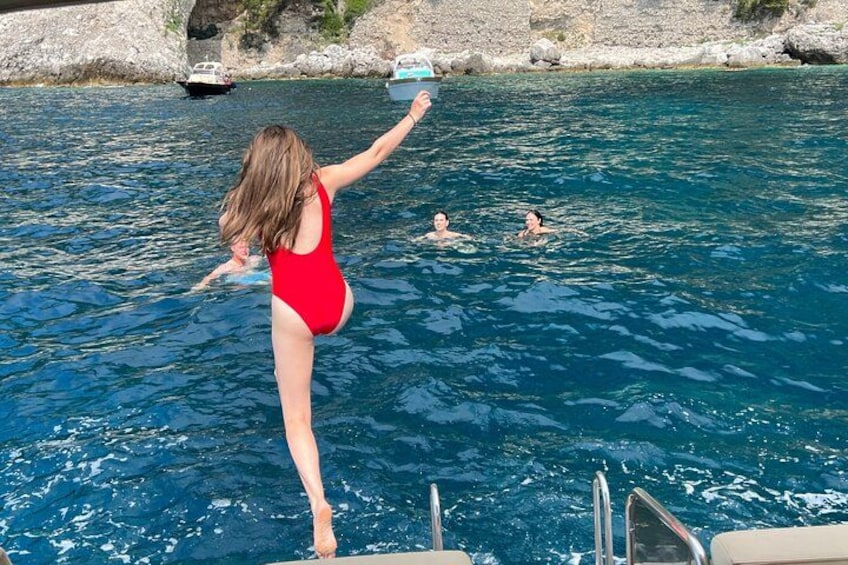 A woman in a red swimsuit jumping into a clear blue pool, with another person swimming in the background. 2