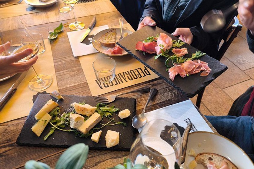 A wooden table with various food items, including cheese, greens, and bread, and a black slate board with the word 'PIQUADRO' visible. 3