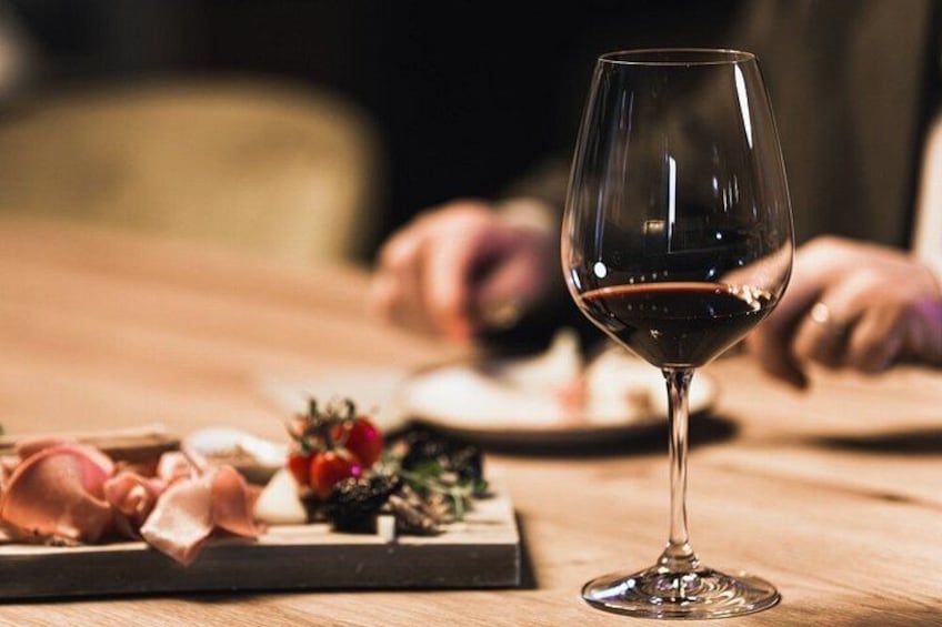 A wine glass with red wine on a wooden table, surrounded by food items. 2