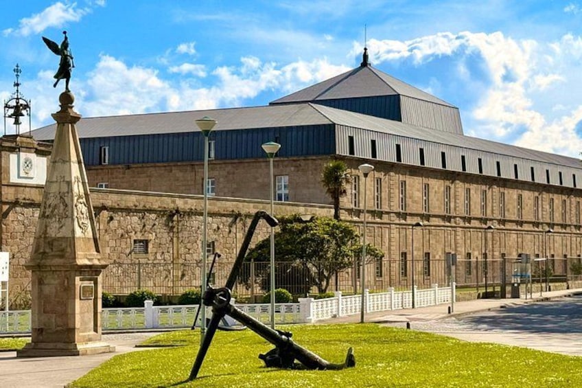 Un edificio grande con techo abovedado, una estatua y un área ajardinada con una escultura. 1