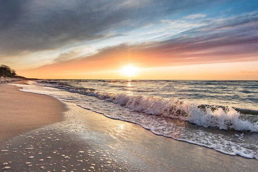 A beach at sunset with waves, a clear sky, and a distant shoreline. 2