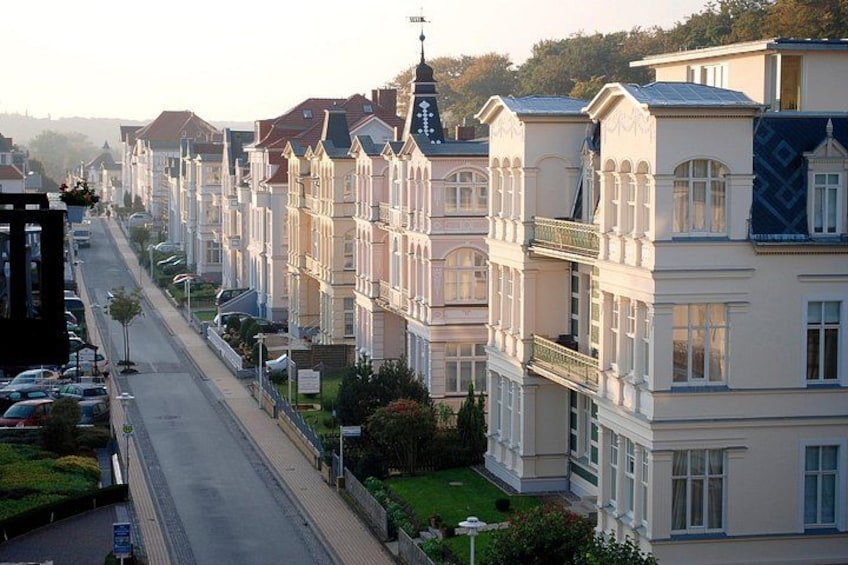 A row of uniform, multi-story houses with balconies, a clear road, and a hilly backdrop. 3