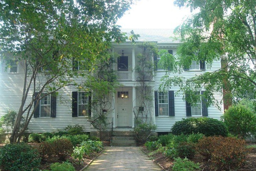 A two-story white house with black shutters, a front porch, and a well-maintained garden. 5
