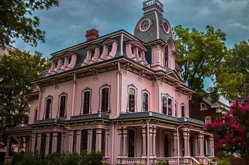A pink Victorian-style house with a clock tower, columns, and a balcony. 1