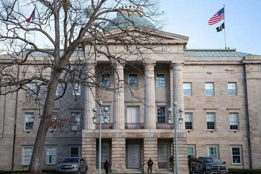 A large, classical building with columns and a dome, an American flag, and a tree in the foreground. 2