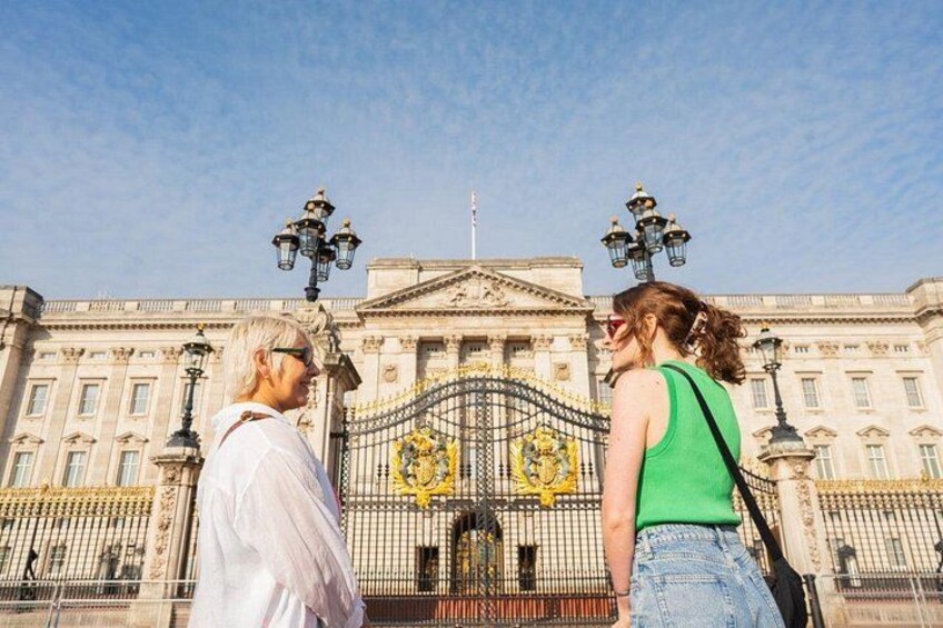 Two people standing in front of a historic building with ornate gates and a clear sky. 4