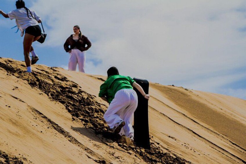 Una persona escala una duna de arena, con otras personas al fondo. 3