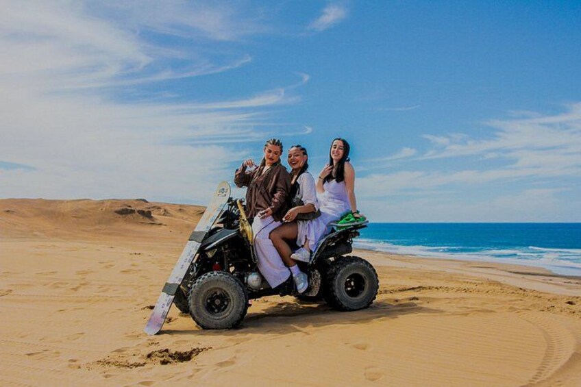Tres personas en un buggy de arena en una playa arenosa, con el océano al fondo. 5