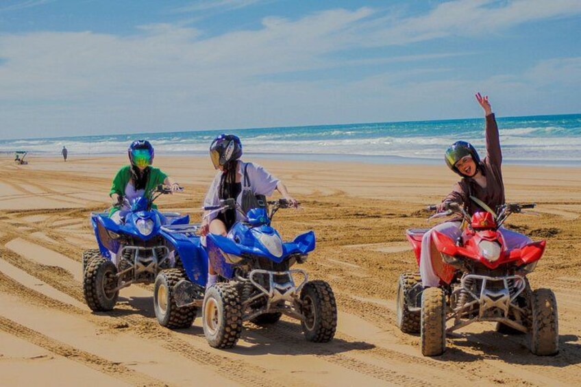 Tres personas conduciendo cuatrimotos en una playa arenosa, con el océano al fondo. 2