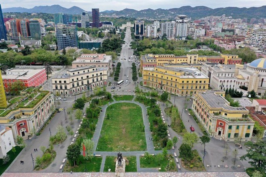 Un paisaje urbano con una plaza central, edificios circundantes y montañas a lo lejos. 2