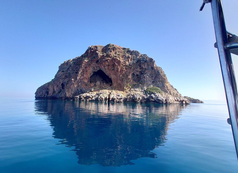 A rocky island with a cave entrance surrounded by calm water. 3