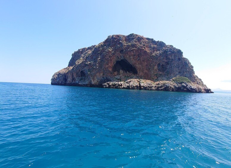 A rocky island with a cave entrance surrounded by clear blue water. 2