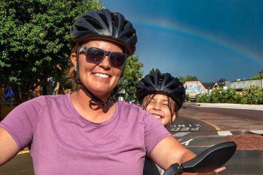 Two people on a bicycle, a rainbow in the background, and a parking lot with a building. 5