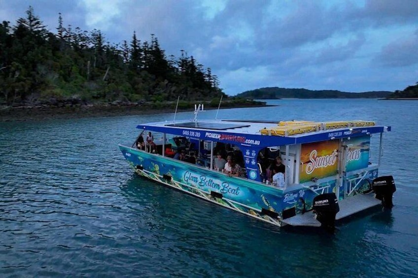 A boat with a blue and yellow exterior, named 'Glenn Bell Boat,' floating on water with a forested shoreline in the background. 2