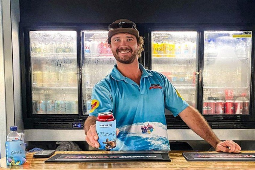 A person standing behind a counter with a beverage in hand, a water bottle, and a menu or card on the counter. 2