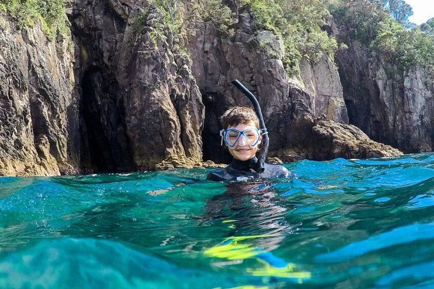 A person snorkeling in clear blue water with rocky cliffs in the background. 3