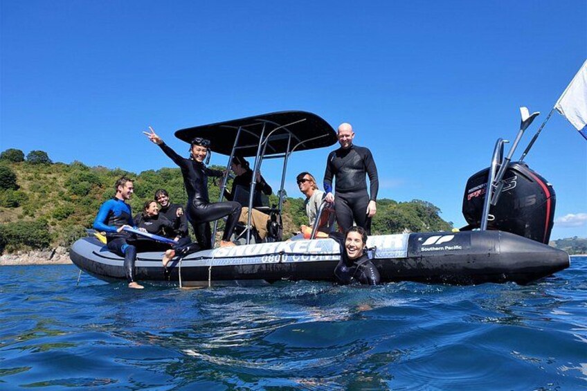 A group of people on a small inflatable boat with a canopy, sailing on clear blue water. 1