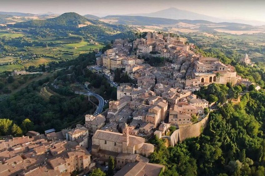 An aerial view of a historic town with a fortified castle, surrounded by lush greenery and rolling hills. 4