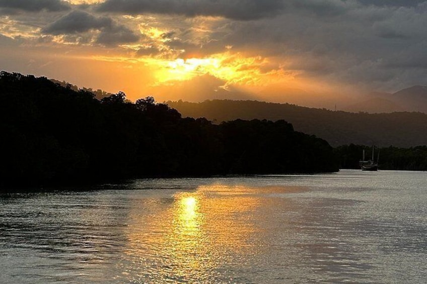 Een zonsondergang boven een rustige rivier, met een boot in de verte en een bebost heuvel in de achtergrond. 5
