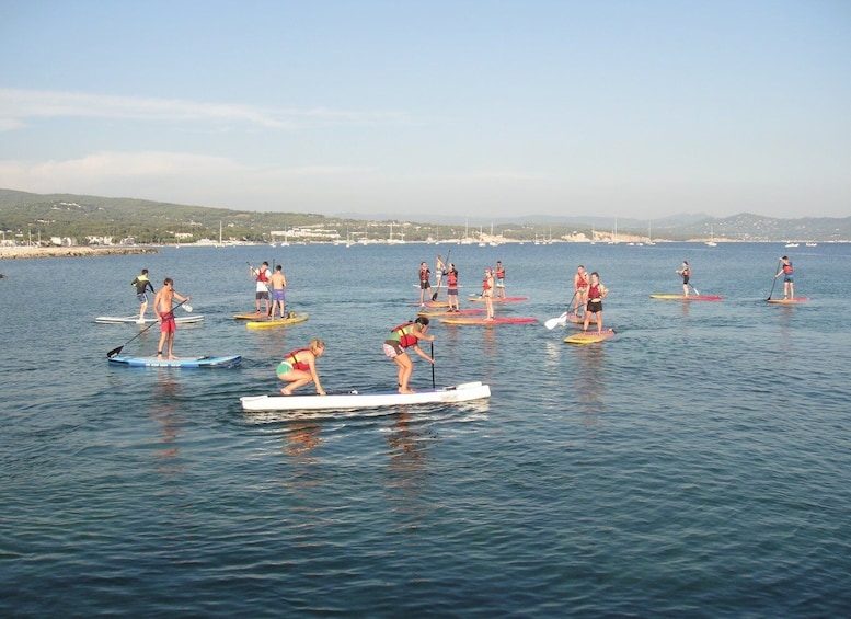 People paddleboarding on calm water with a clear sky and distant hills. 2