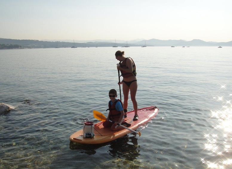 Two people on a paddleboard in calm waters with boats in the background. 3