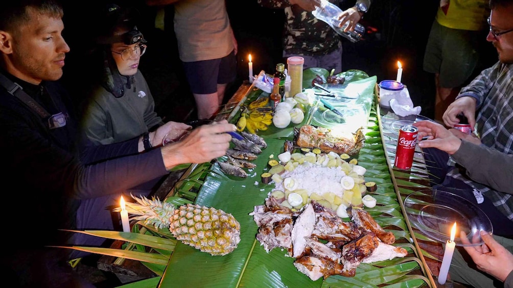 A communal meal with various dishes, including fish, rice, and fruits, served on a long table with candles. 4