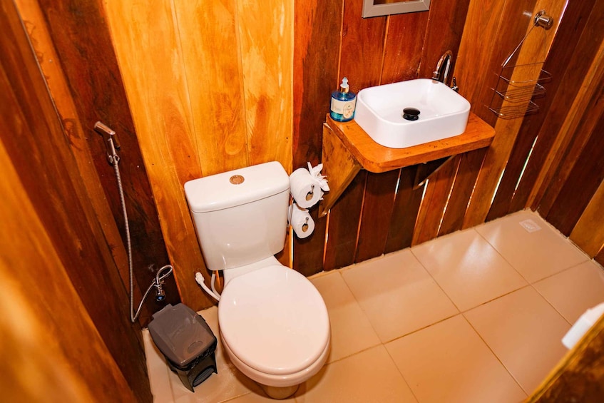 A compact wooden bathroom with a white toilet, a small sink, and a toilet paper holder. 5