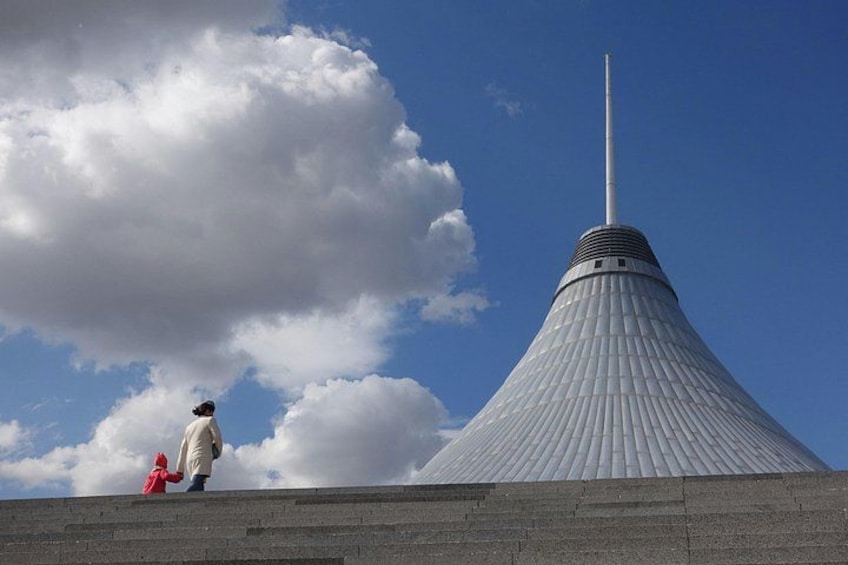 A large, conical structure with a tall spire, a person in a red jacket, and a partly cloudy sky. 4
