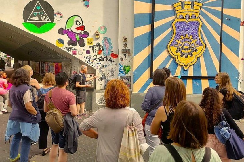 Un grupo de personas en un espacio público con grafitis y un gran emblema en la pared. 3