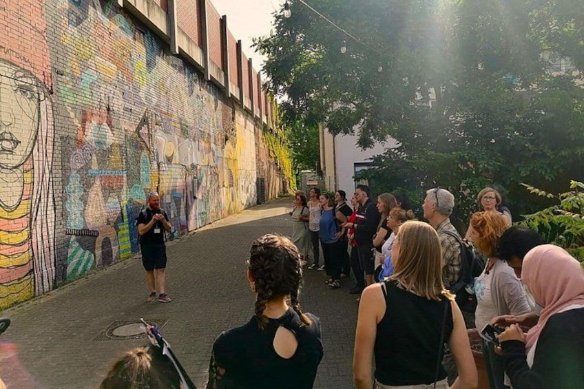 Un grupo de personas de pie en una calle con un mural colorido en la pared. 2