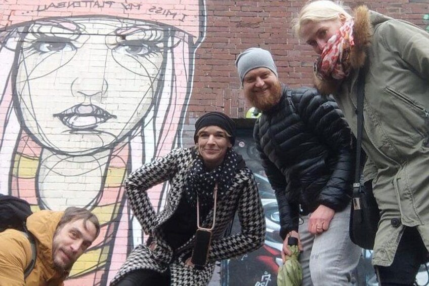 En grupp människor som står framför en väggmålning med ett ansikte avbildat. 3