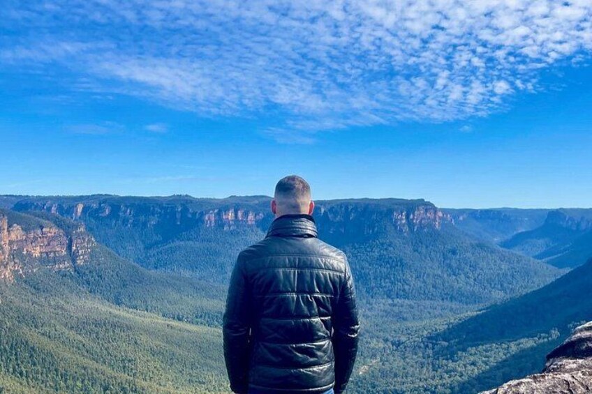 A person standing on a cliff overlooking a canyon with steep cliffs and dense forest. 3