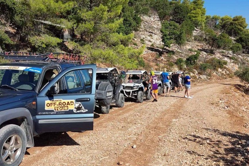 A group of people and vehicles on a dirt road with a rocky hillside in the background. 1