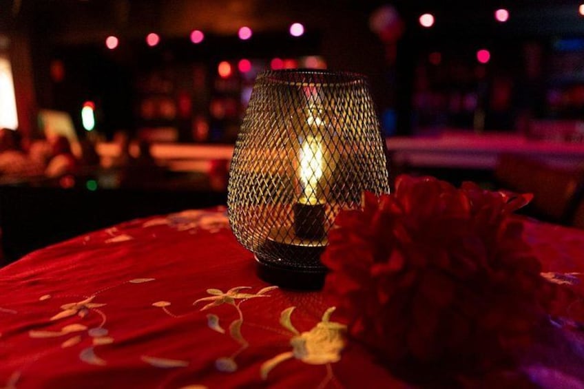 A lit candle in a glass holder on a red tablecloth with a red flower. 5