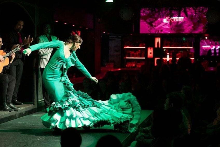 A person in a green dress performing on a stage with a guitar player in the background. 2