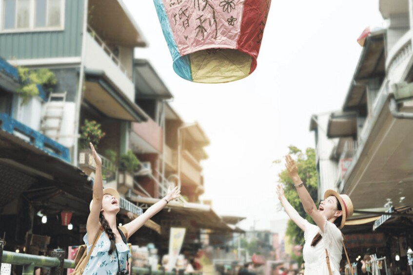 Two people raising their hands towards a hanging paper lantern with Chinese characters. 4