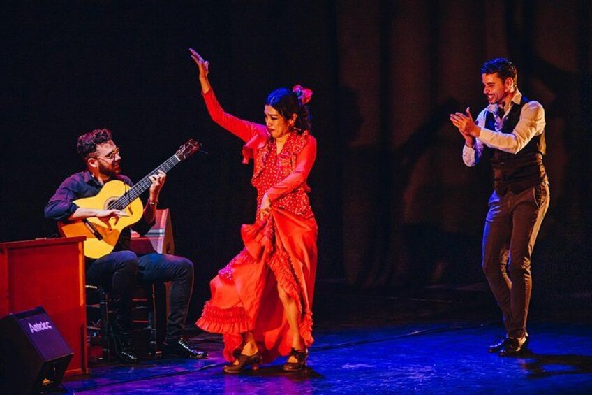 A stage with three people, one playing a guitar, another dancing, and a third clapping. 3
