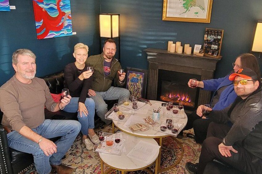 Un grupo de personas sentadas alrededor de una mesa, con bebidas, una chimenea y obras de arte en las paredes. 2