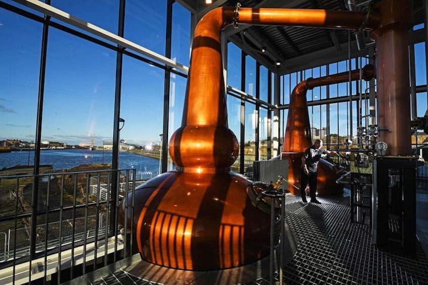 A distillery with large copper stills and a view of a river. 4