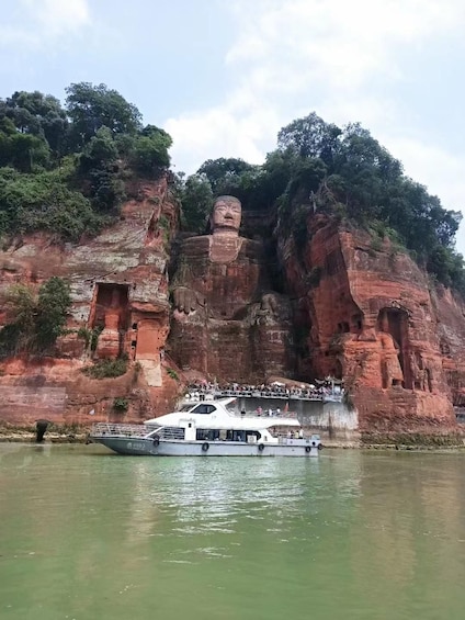 A large rock formation with a statue on top, a boat in the foreground, and a viewing platform with people. 5