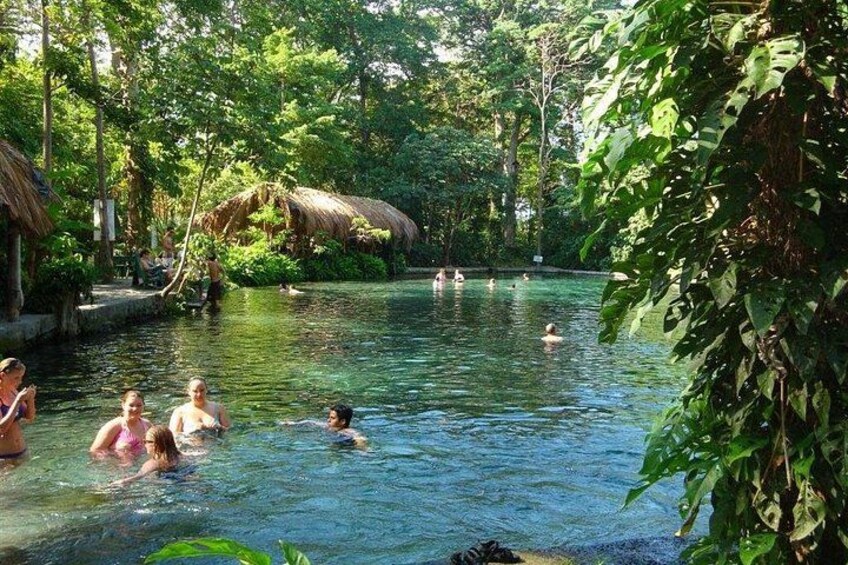 A natural pool surrounded by lush greenery and thatched-roof huts. 4