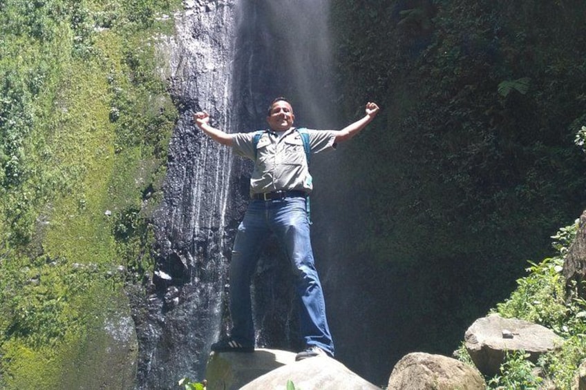A person standing on a rock with arms outstretched in front of a waterfall. 3