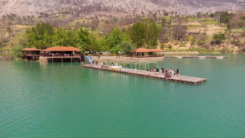 A pier extending into a lake with people on it and two buildings with red roofs. 3