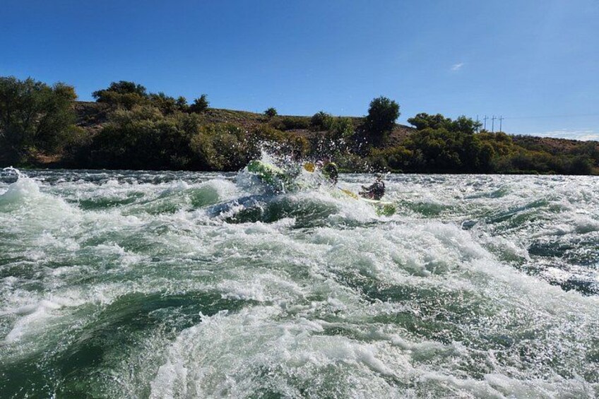 A river with white water rapids, a kayaker, and a hilly landscape with trees in the background. 4