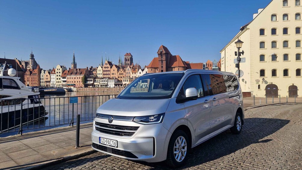 Hopeanvärinen Volkswagen-pakettiauto on pysäköitynä kanavan varteen, ja taustalla näkyy historiallisia rakennuksia. 3