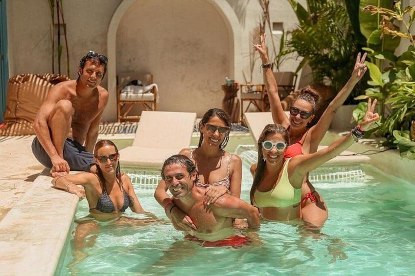 A group of people in a swimming pool with a tiled deck and lounge chairs. 4
