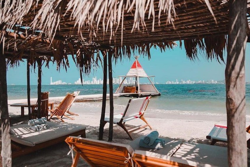 A beach with thatched umbrellas, lounge chairs, and a small boat with a red and white sail. 3