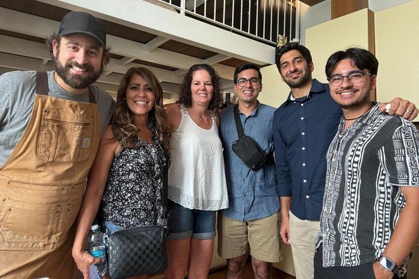 Un grupo de personas de pie en el interior, algunas vestidas con ropa informal, con una escalera al fondo. 4